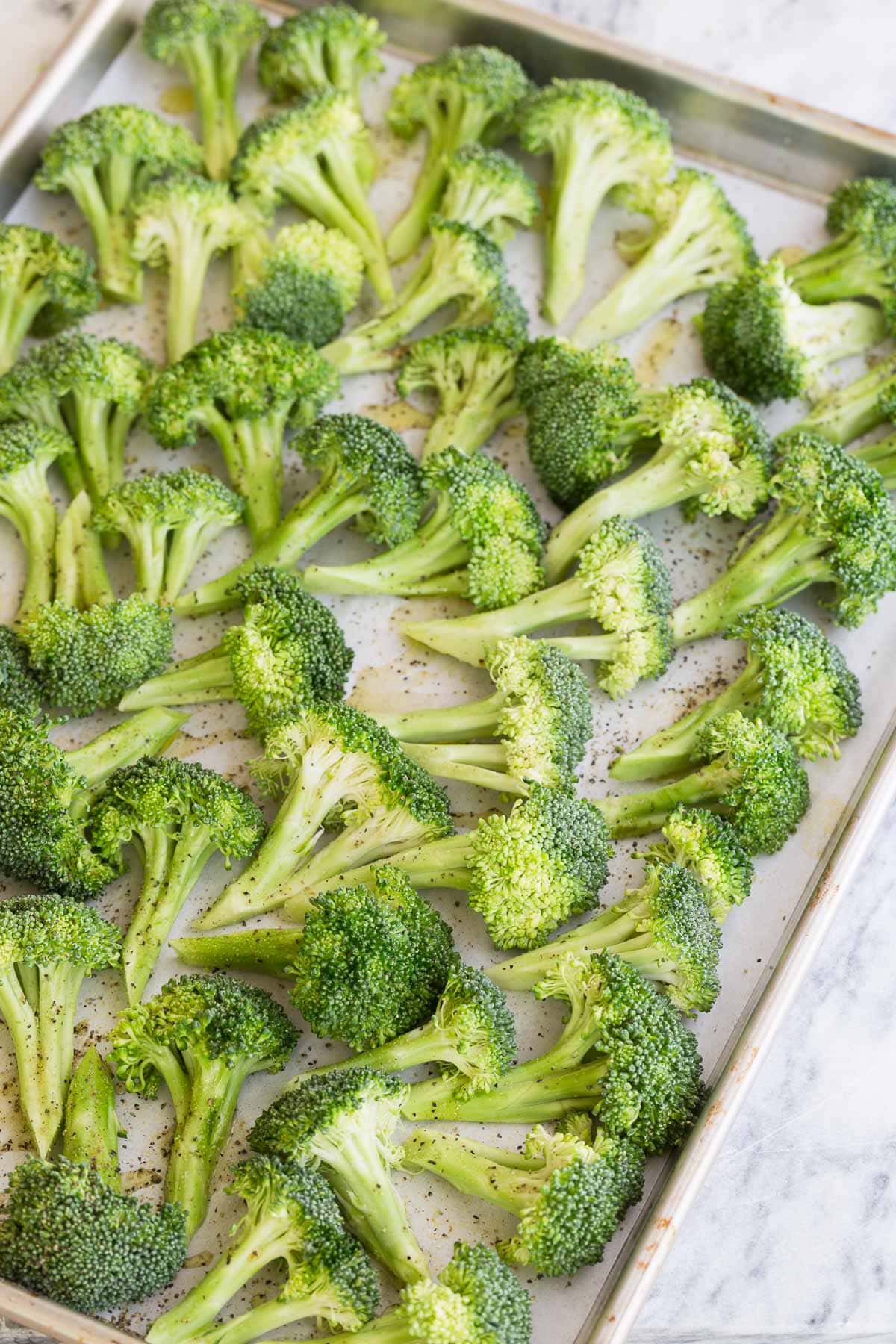 Broccoli florets arranged flat on a baking tray for roasting.