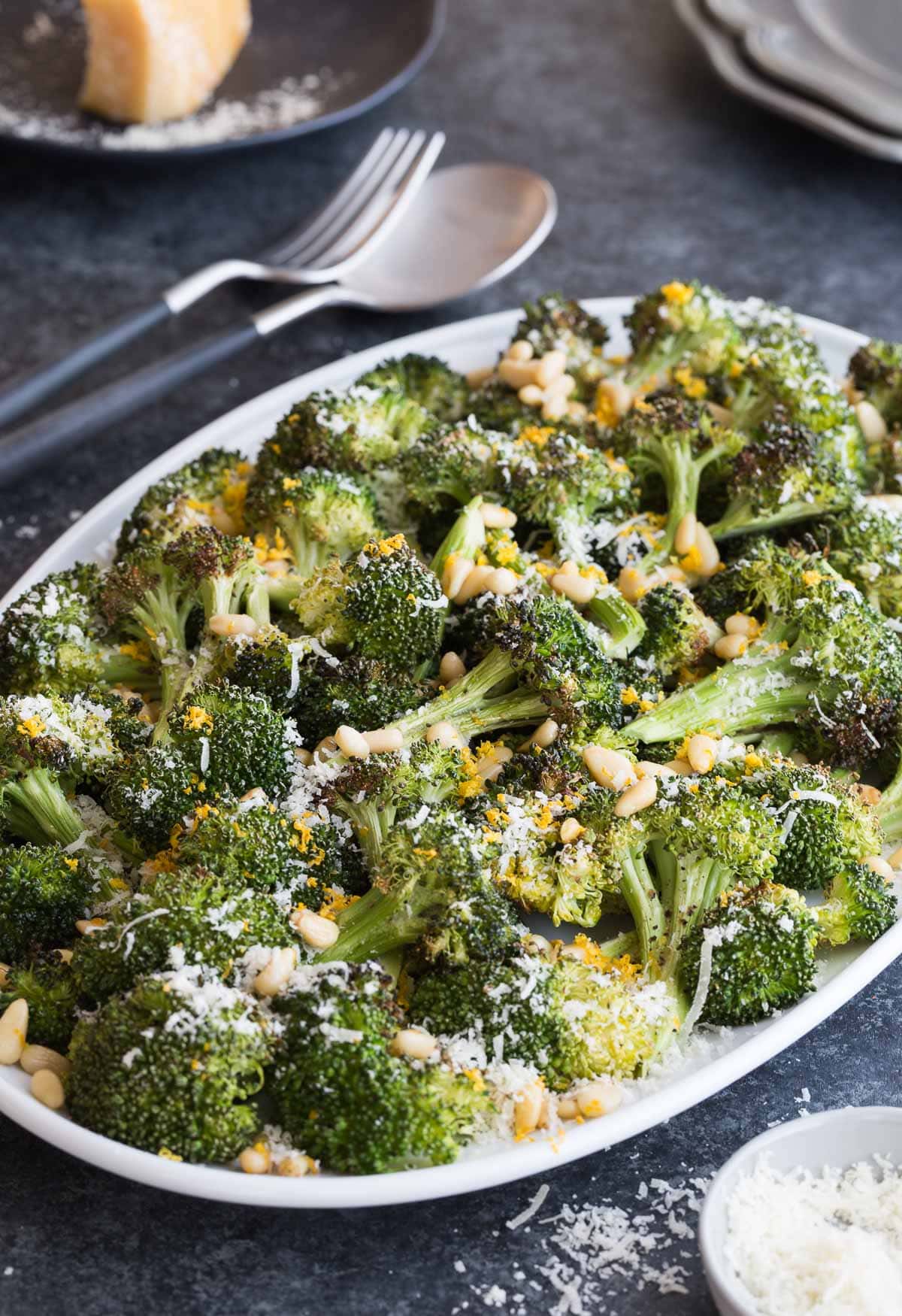 A serving platter of green broccoli spears with parmesan cheees and lemon zest garnish.