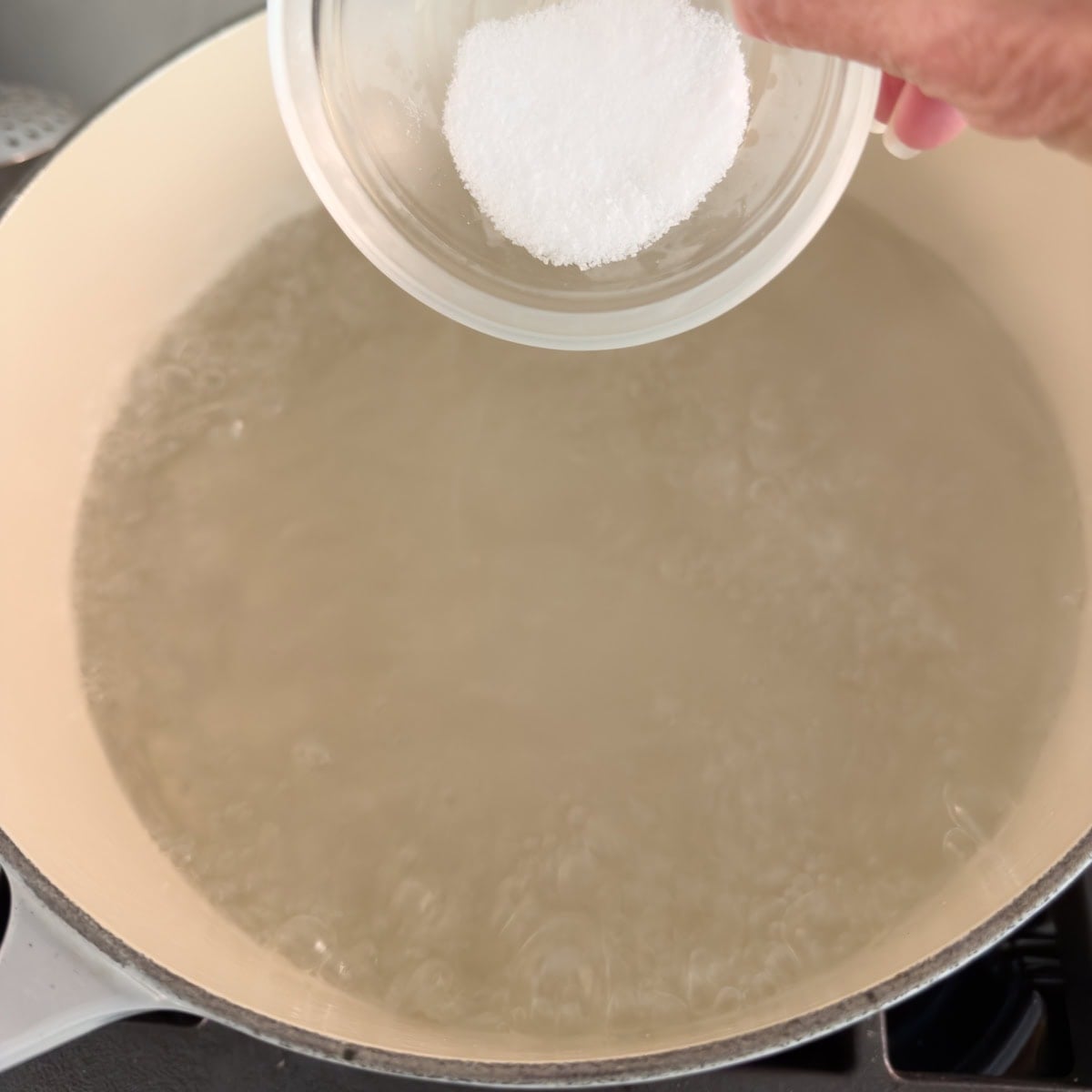 A pot of boiling water with salt being added to it to hard boil eggs.