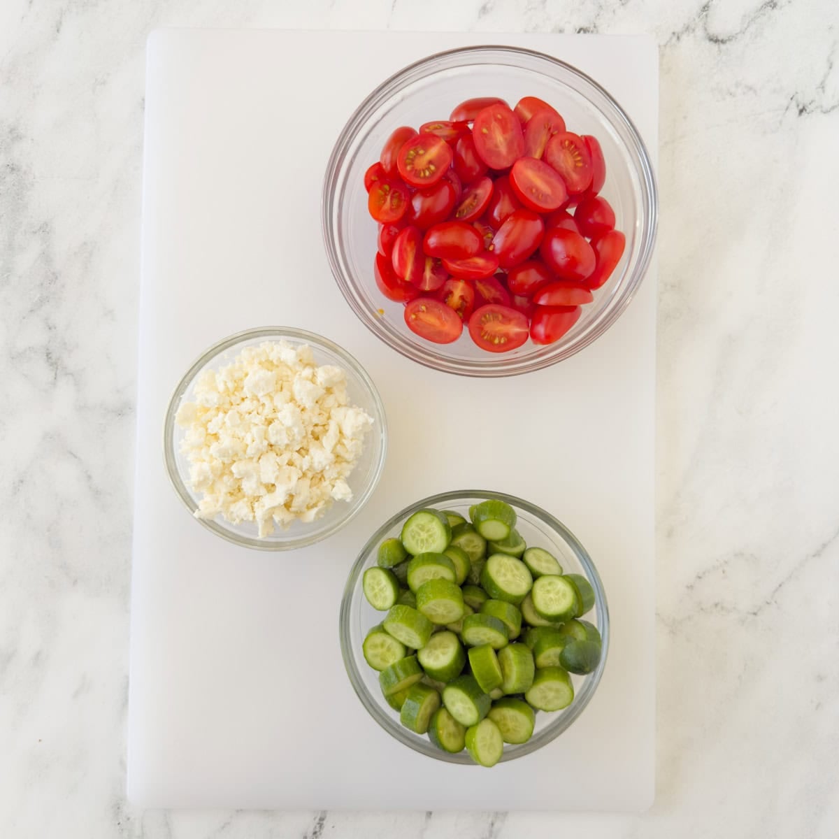 Bright red grap tomatoes, chopped mini cucumbers, and crumbled feta cheese for a Greek salad.