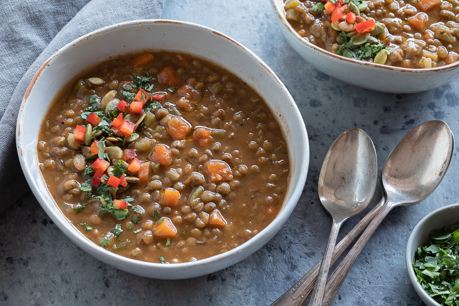 A bowl of lentil soup with garnishes and spoons, ready to serve.
