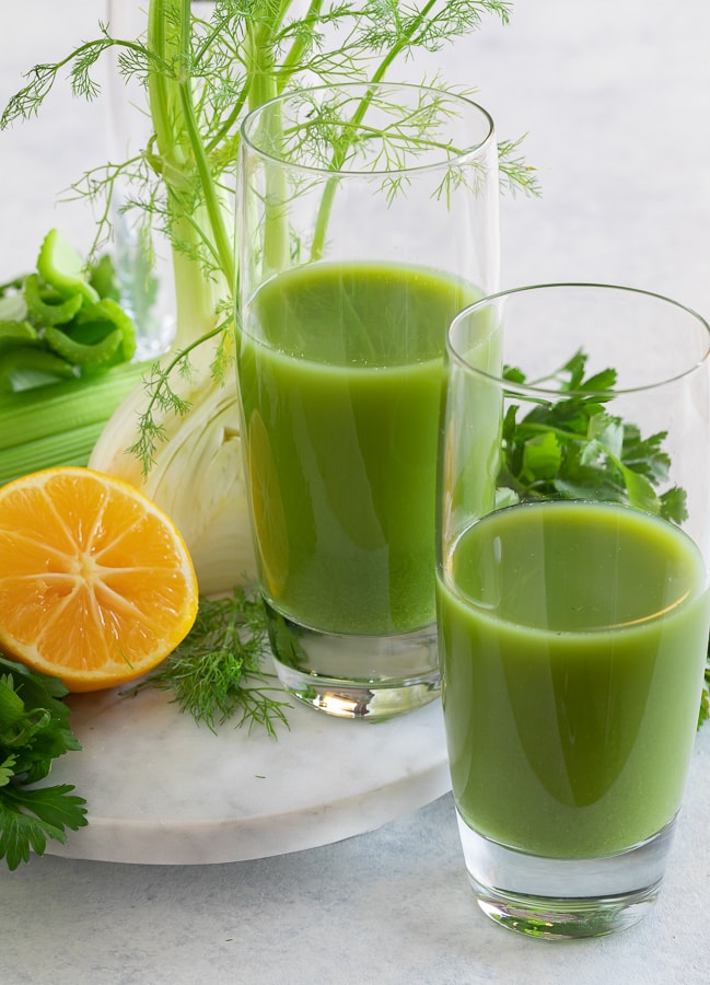 Two glass of green juice with a lemon half.