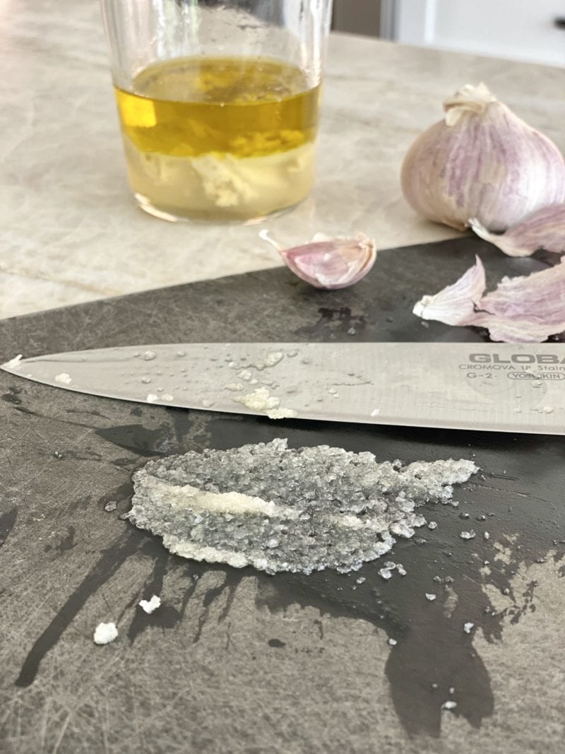 Smearing chopped garlic into a paste on a cutting board.