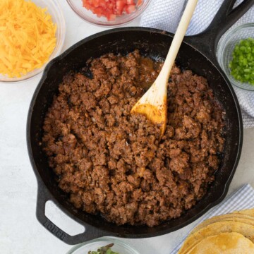 Taco meat in a cast iron pan with fixings for tacos around it.
