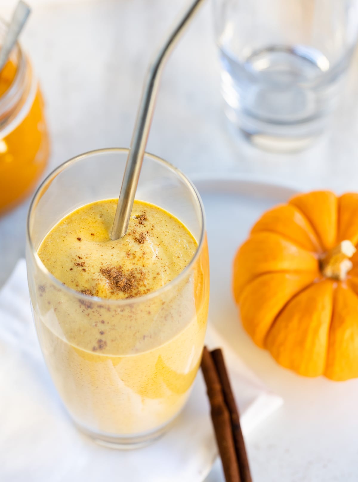 A beautiful orange colored creamy pumpkin smoothie in a tall glass with a steel straw. 