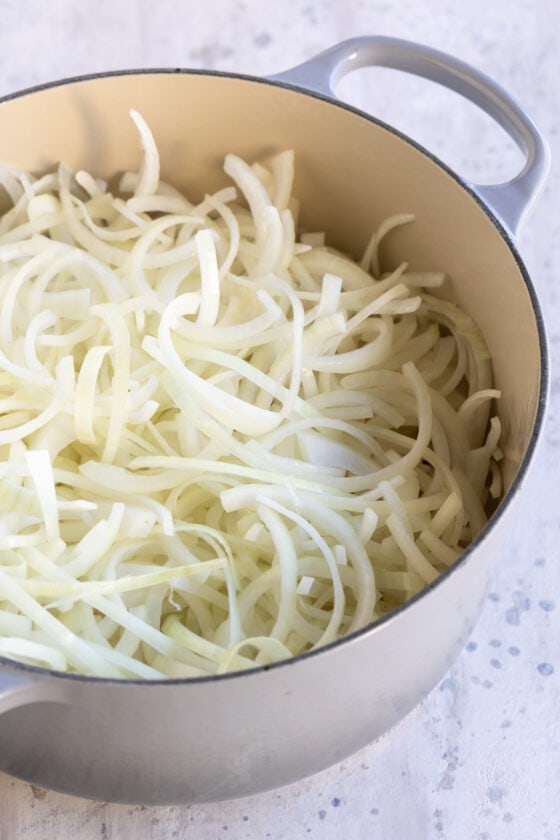 Thinly sliced onions in a light gray dutch oven.