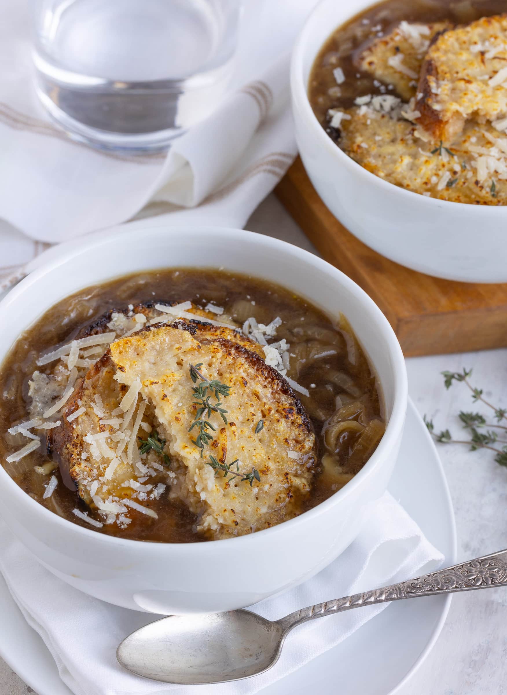 French onion soup in a white bowl with golden cheesy croutons and fresh thyme.