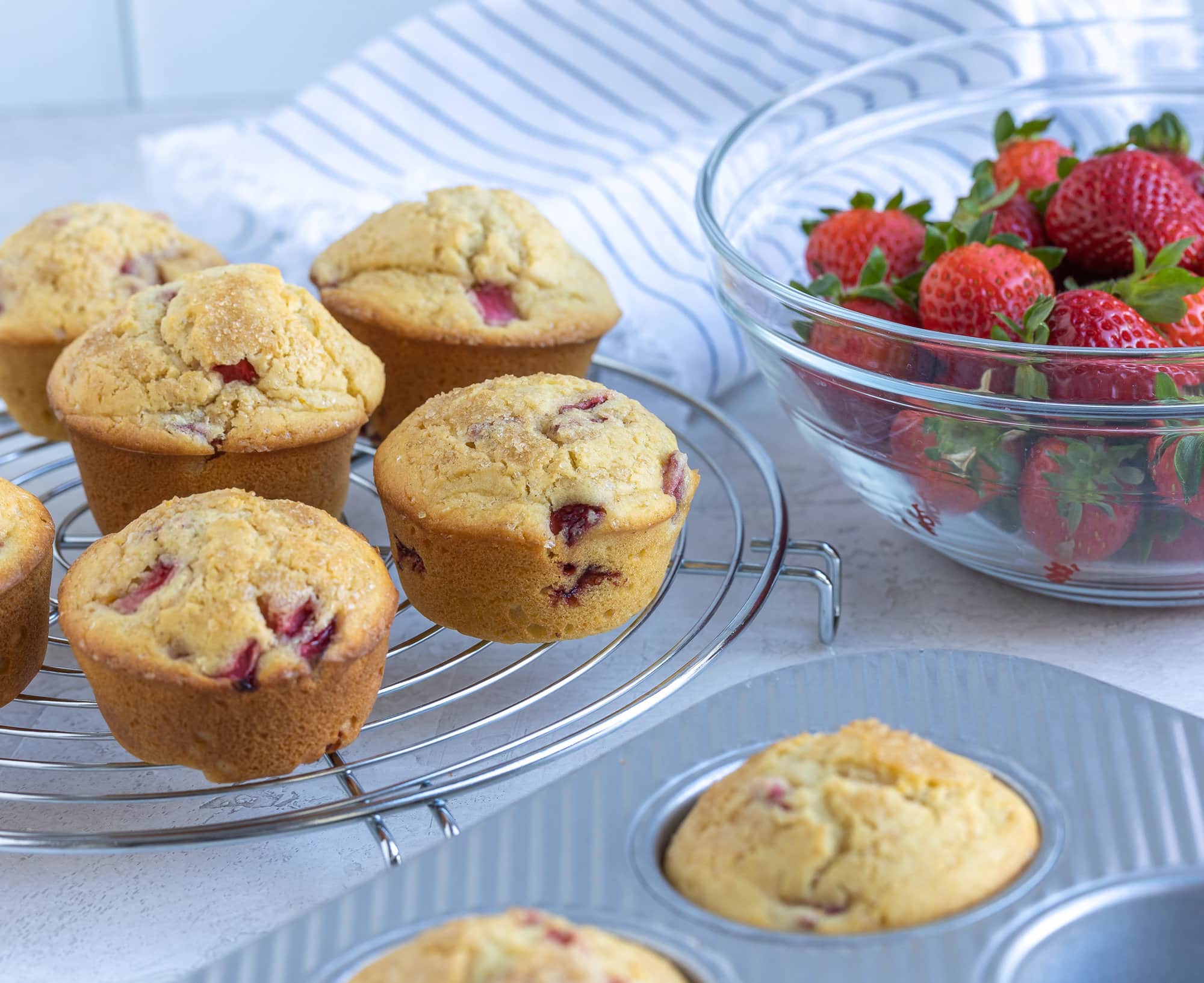 Golden muffins cooling on a rack with a bowl of berries.