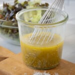 Golden Italian salad dressing in a jar with a silver whisk.