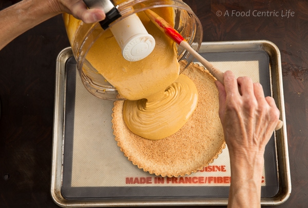 Pouring pumpkin filling into a tart crust before baking.