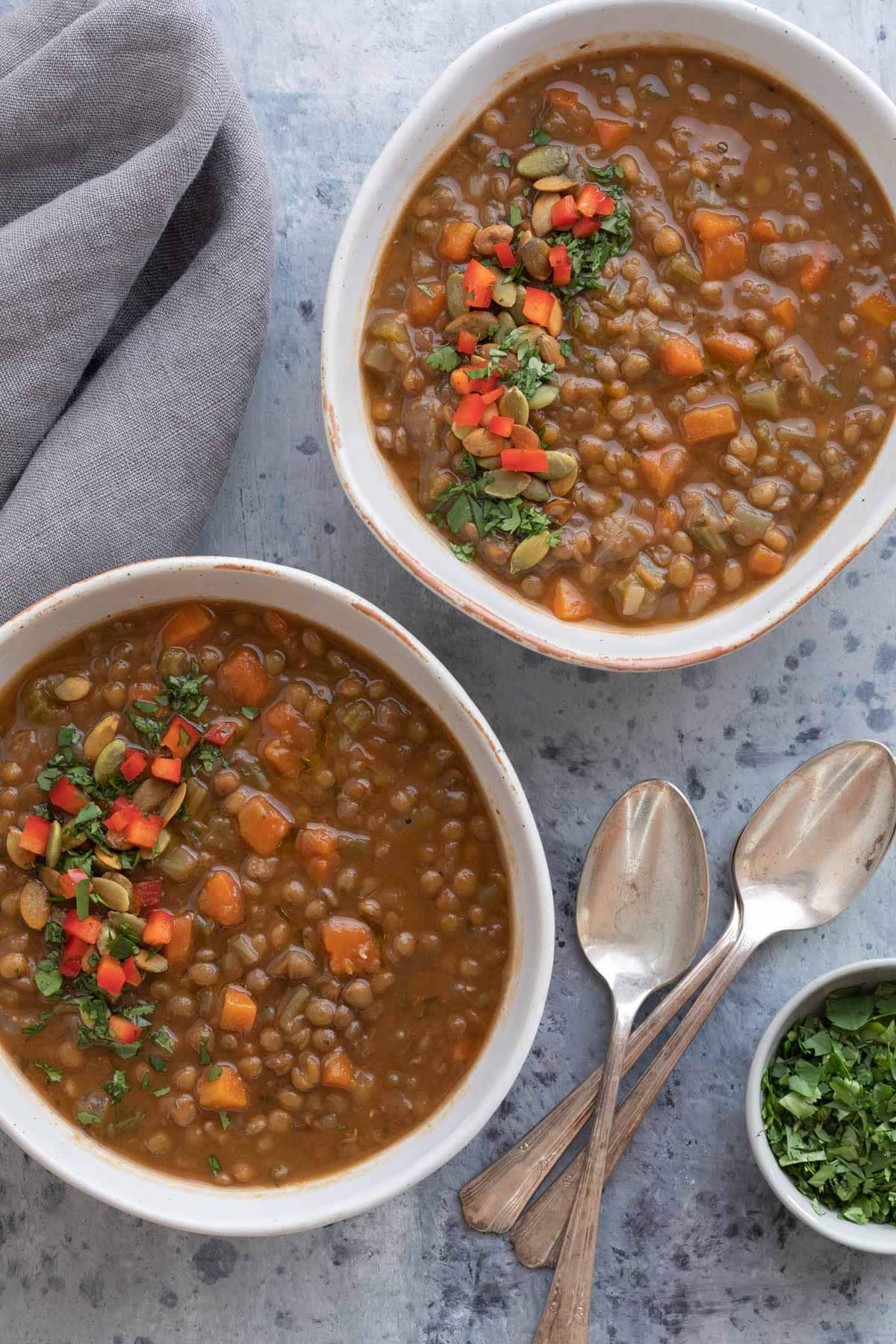 Lentil soup with vegetables in bowls with spoons and parsley.