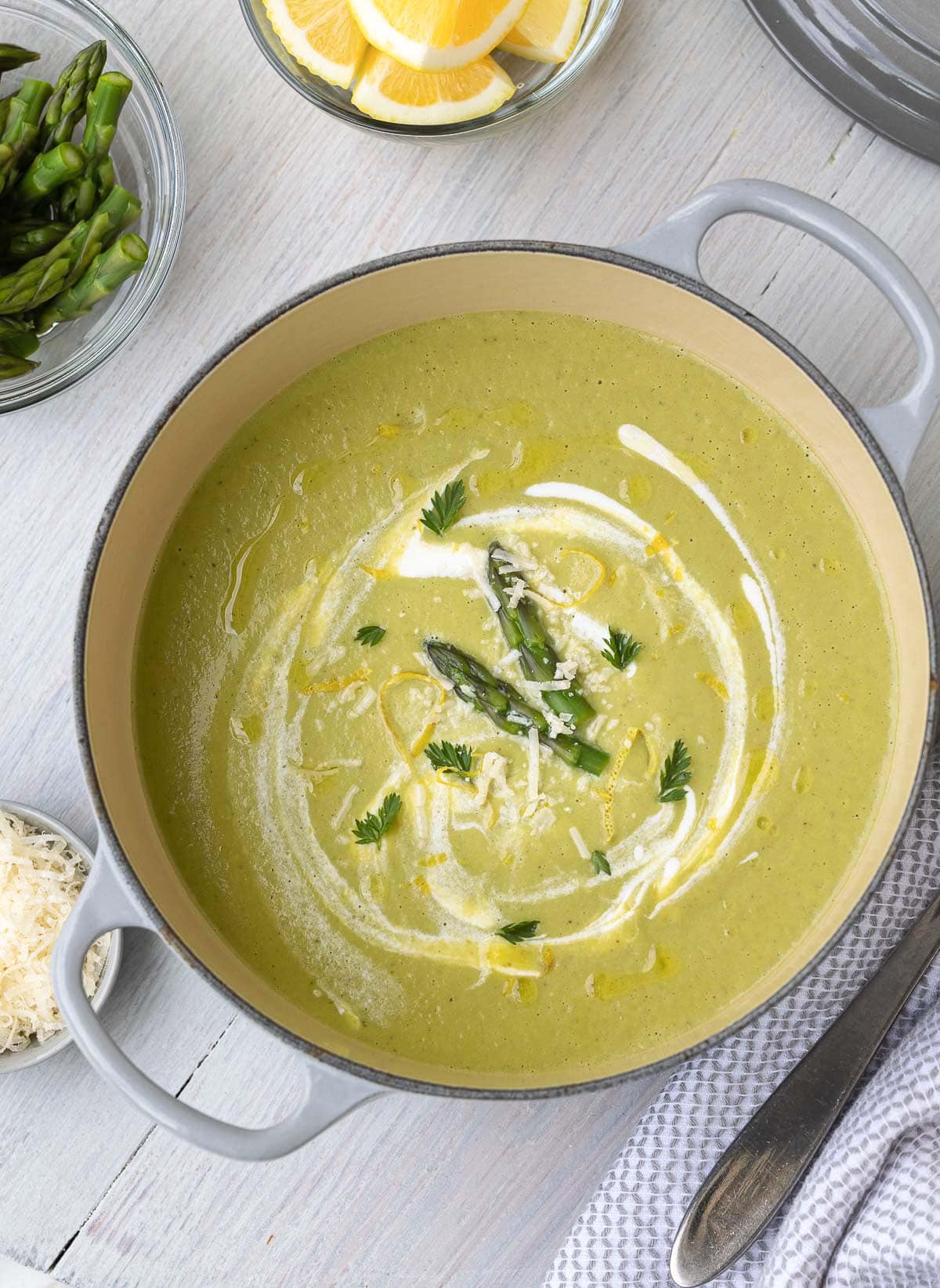 Bright green and creamy asparagus soup in a gray pot with garnishes. 