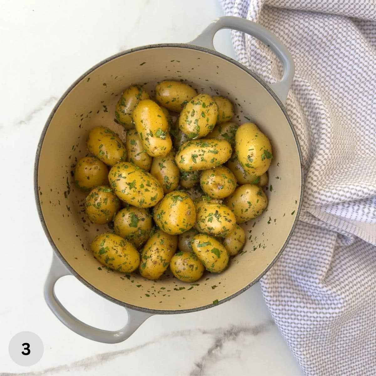 Cooked baby potatoes covered in fresh herbs in a pot.