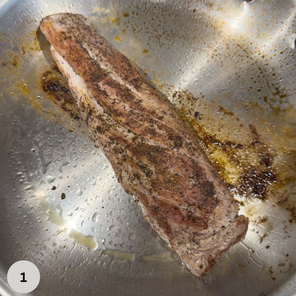 Searing pork tenderloin in a stainless steel fry pan. 