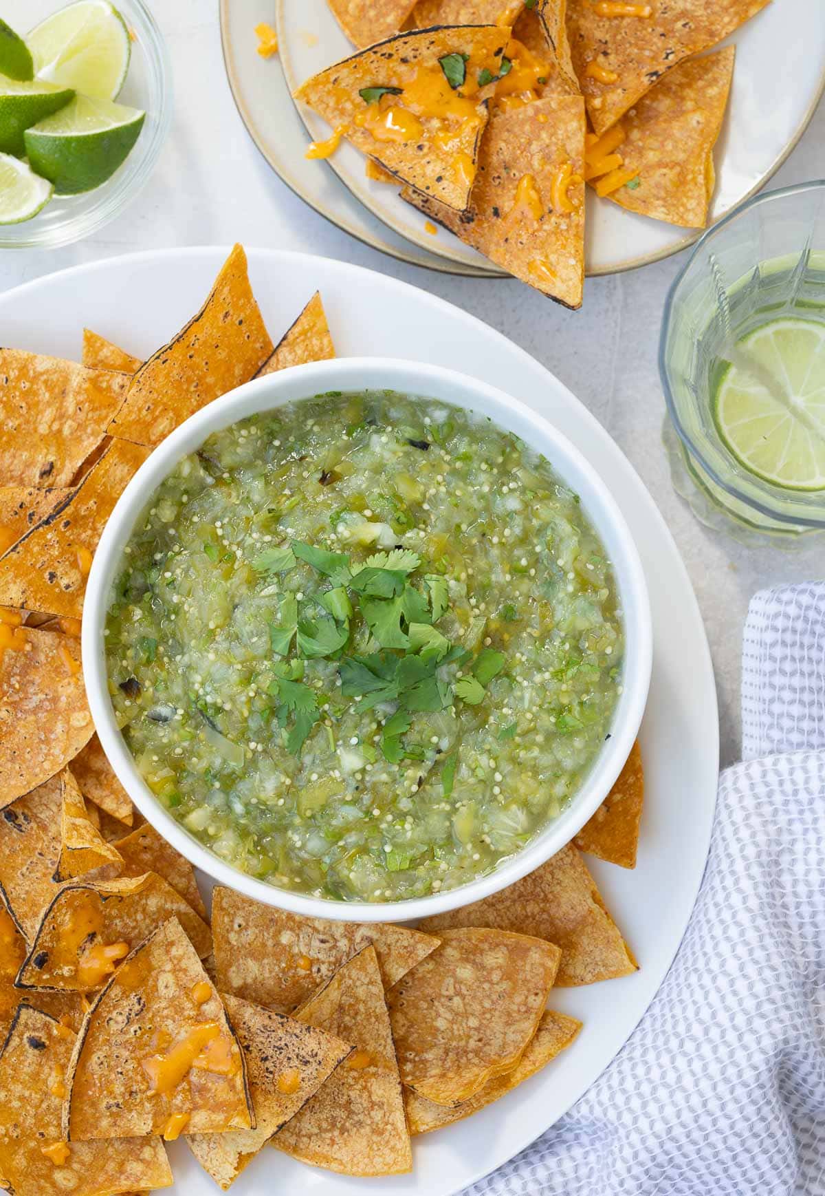 A bowl of green salsa verde with a platter of crisp chips with cheese.