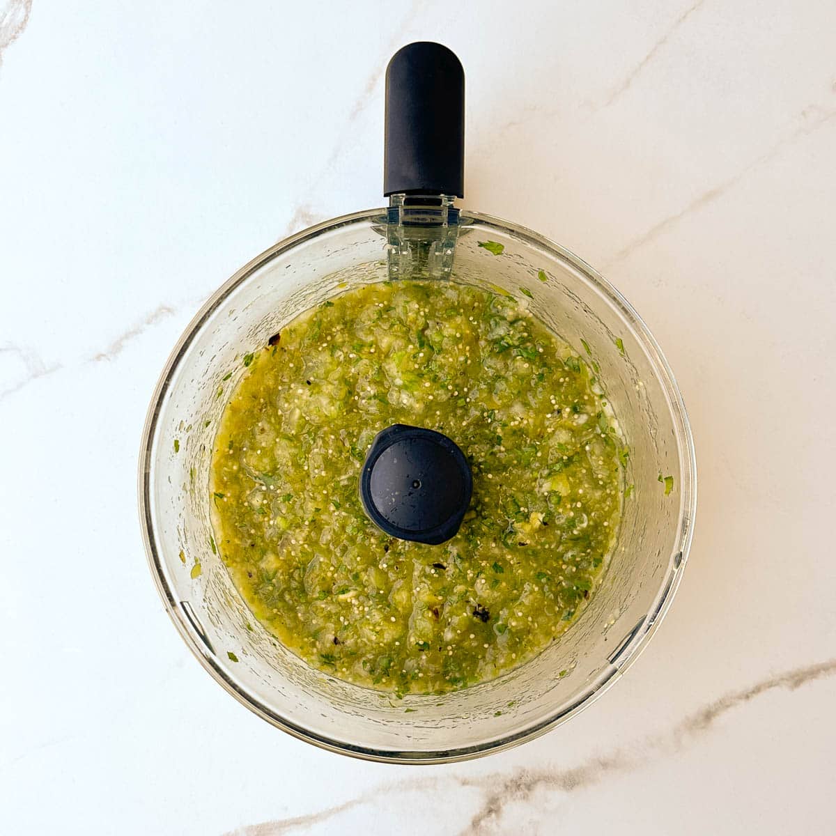 Pureed salsa verde, still a bit chunky, ready to serve, in a food processor.
