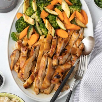 A platter of sliced glazed teriyaki chicken with broccoli, carrots and zucchini.