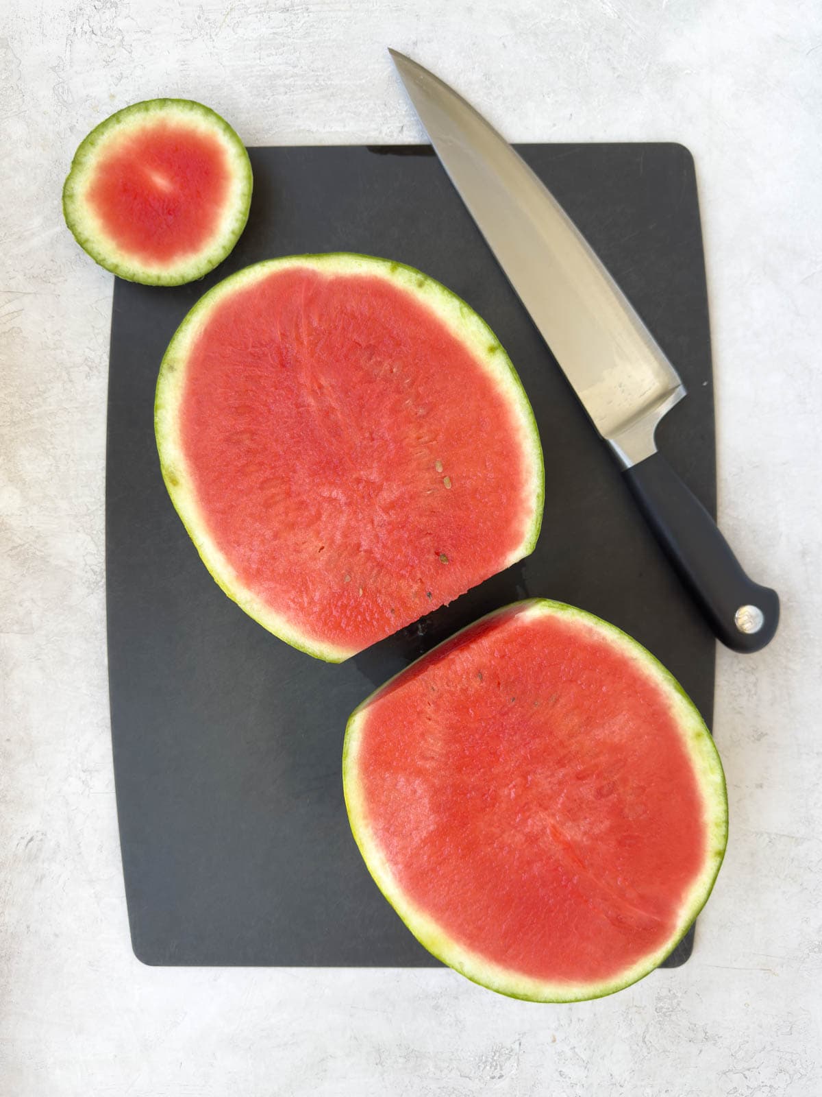 Red seedless watermelon cut on half on a black cutting board.