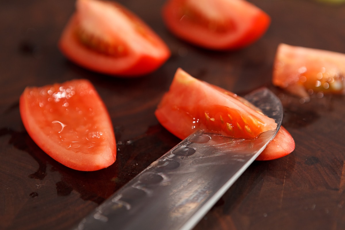 Slicing seedy centers out of tomatoes on a walnut cutting board with a sharp knife.