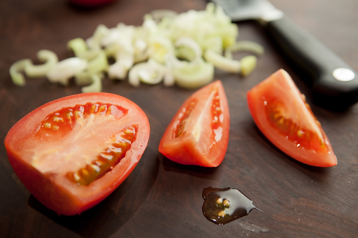 First step for cutting tomatoes, top sliced off and cut it in half, then quarters.