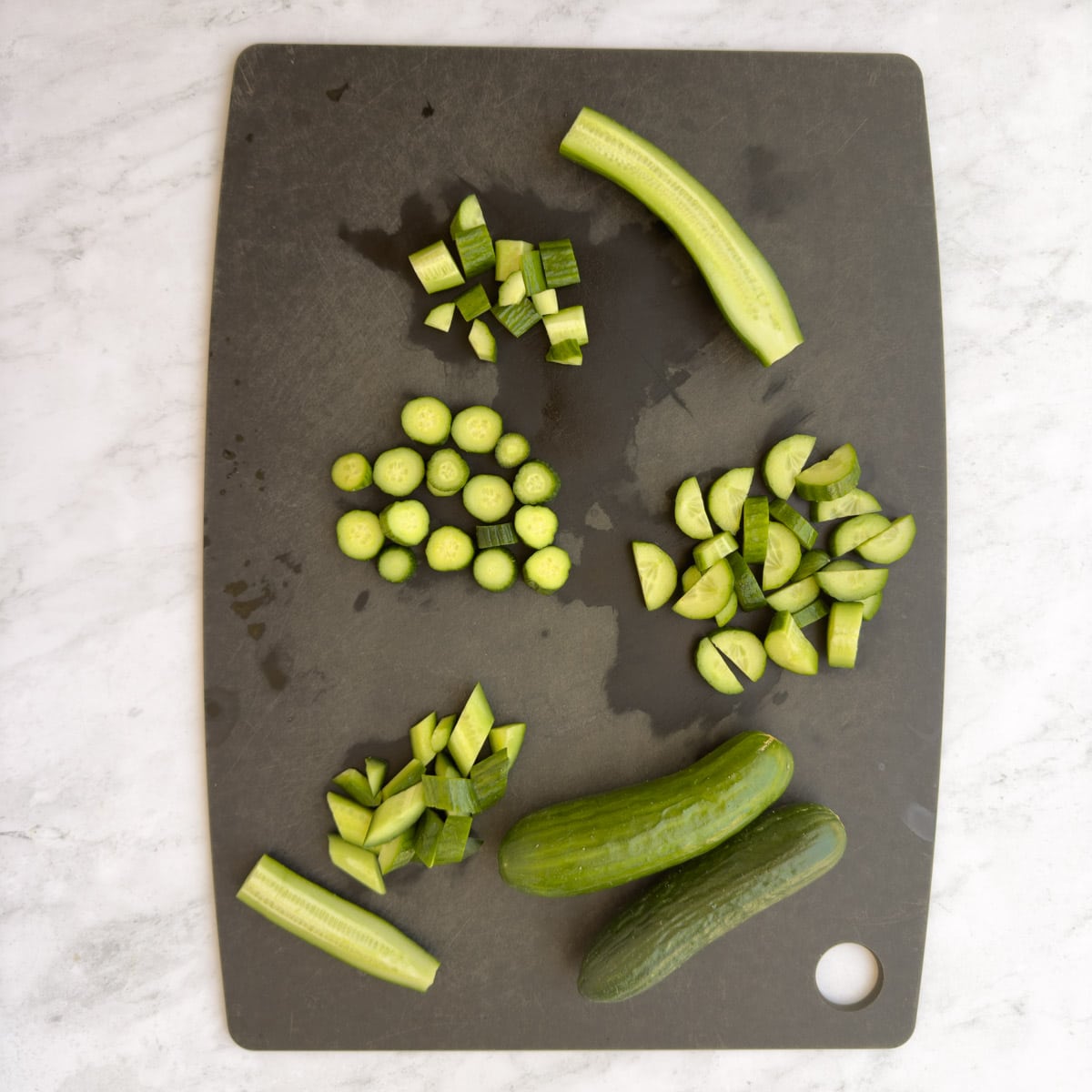 Cucumbers on a black cutting board cut in different ways.