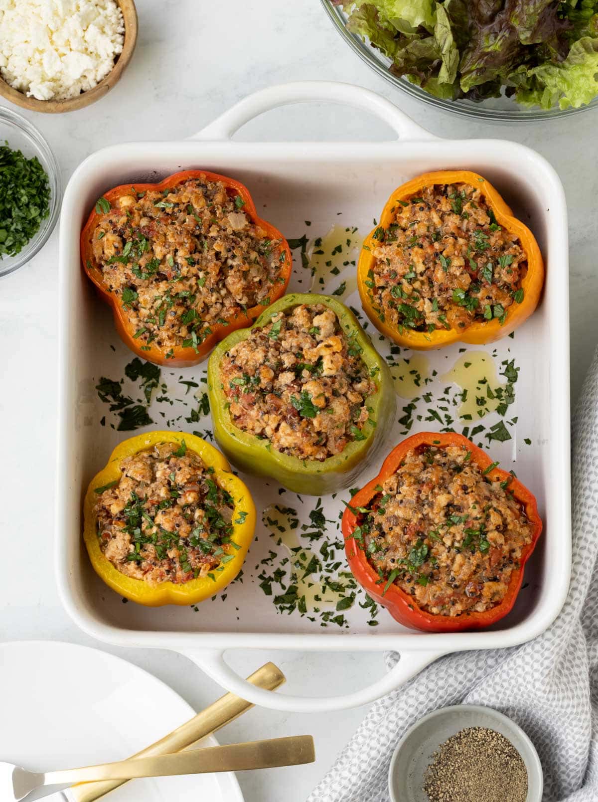Red, yellow, green, and orange stuffed peppers in a white baking dish.