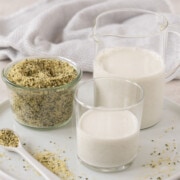 White round platter with a glass of hemp seed milk, a pitcher, and hemp seeds.