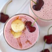 Top down shot of a deep pink cherry smoothie in a tall glass with banana and a cherry.