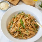 A white bowl of sun-dried tomato pesto pasta with basil and parmesan garnish.