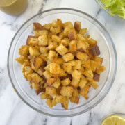 A bowl of golden baked croutons in a glass bowl on a counter.