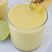 A bright yellow mango pineapple smoothie in a glass with lime and fruit wedge.