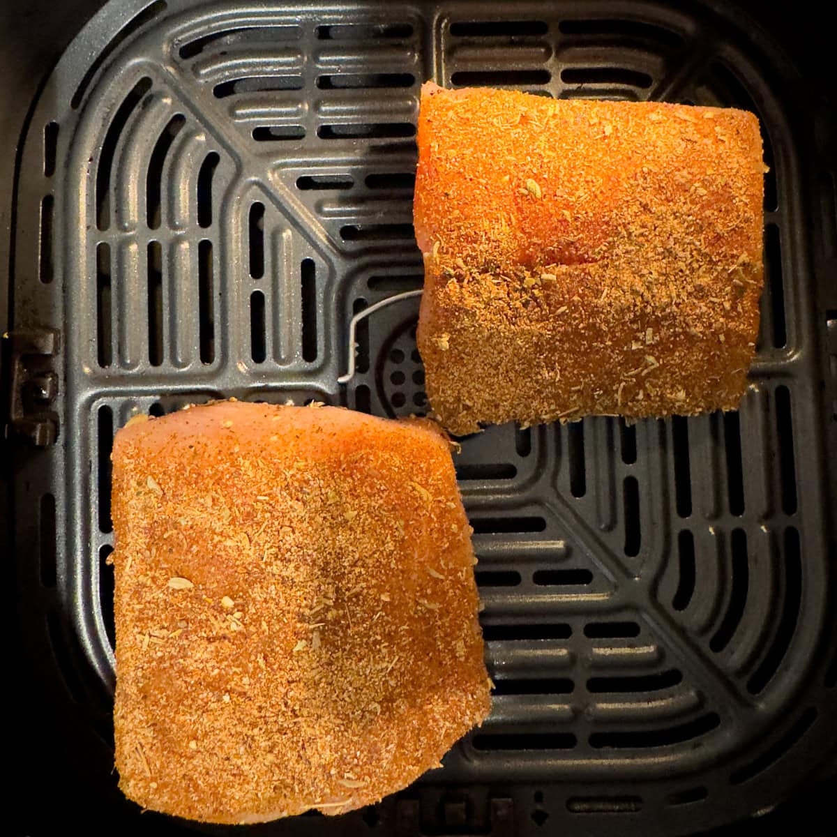 Two fish filets coated with blackening seasoning in an air fryer basket.