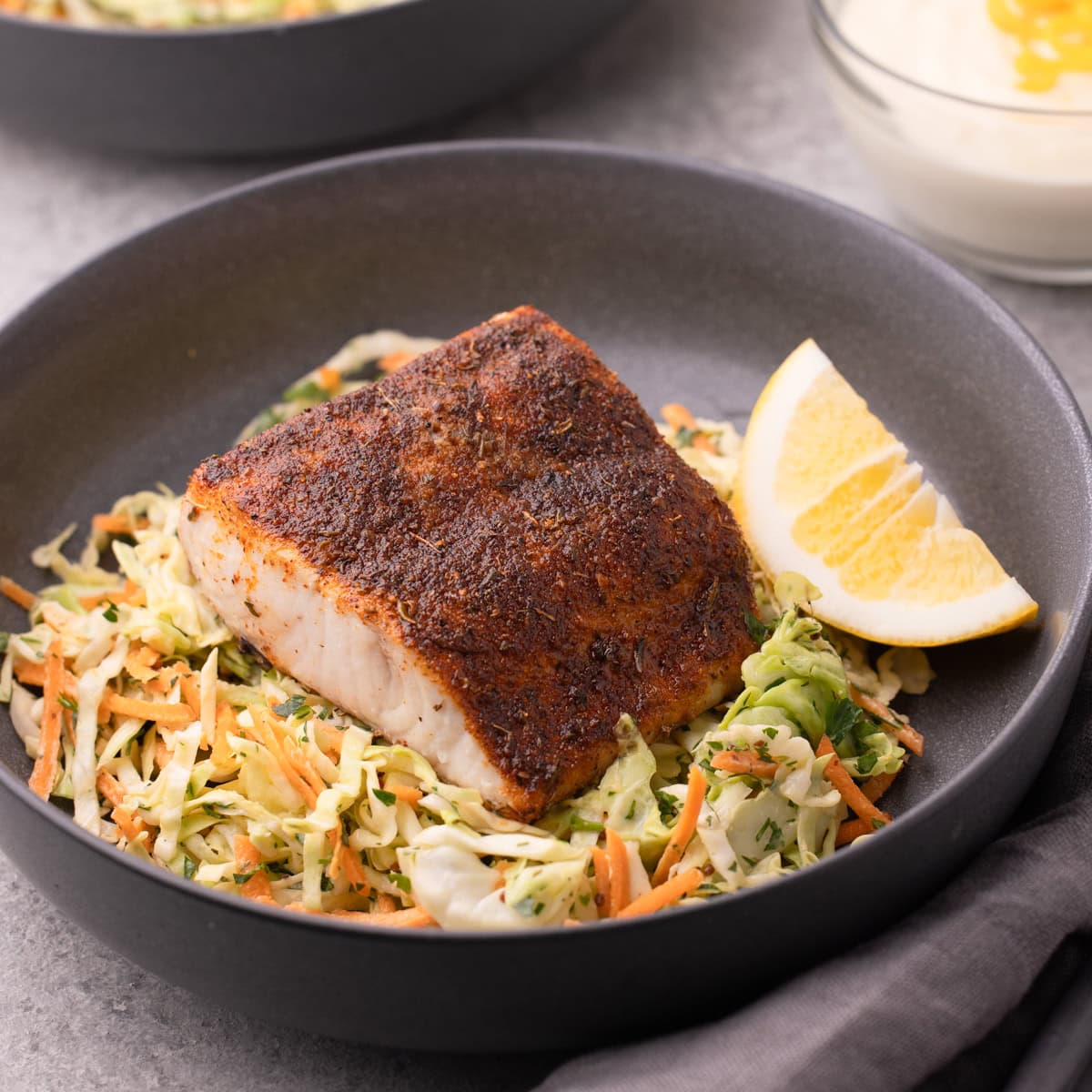 A shallow gray bowl with coleslaw topped with air fryer mahi mahi with a blackening seasoning.
