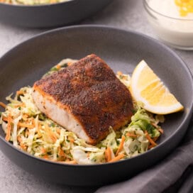 Crusty topped blackened fish filet on top of coleslaw in a gray bowl.