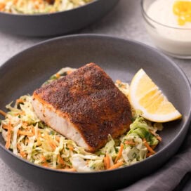 A gray bowl filed with colorful coleslaw topped with blackened mahi mahi filet and a lemon wedge.