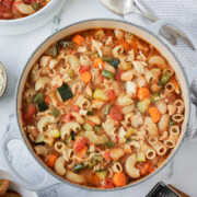 A dutch oven full of chicken minestrone soup with a bowl on the side.