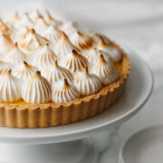 A beautiful lemon tart with piles of piped meringue on top of a cake plate.