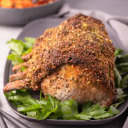 A golden crusted pork rib roast on a gray platter with fresh green parsley.