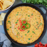 Cast iron pan of cheesy queso dip with cilantro, tortilla chips, and jalapeno garnish.