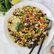 Bright colored avocado , black bean, and corn salad with tomatoes and jalapenos in a white bowl.