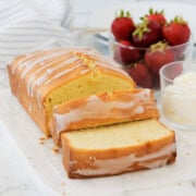 Sliced of golden pound cake with strawberries and a small bowl of whipped cream.