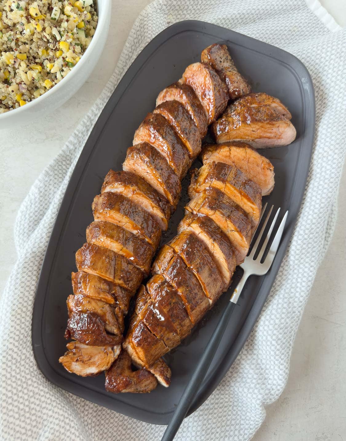 Sliced pork tenderloins glazed with bbq sauce on a gray platter with a salad beside.