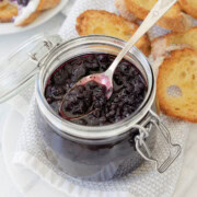 Deep purple blueberry compote in a glass jar with a silver spoon.