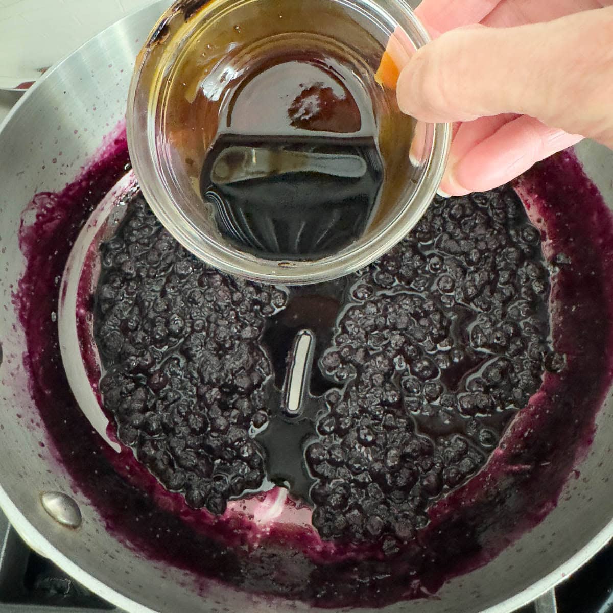 Adding balsamic vinegar to a pan of cooking blueberries.