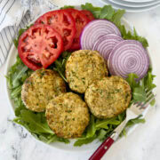A plate of air fried chicken patties with lettuce, tomatoes, and red onion.