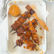 Tray of grilled harissa chicken on bamboo skewers with harissa sauce.
