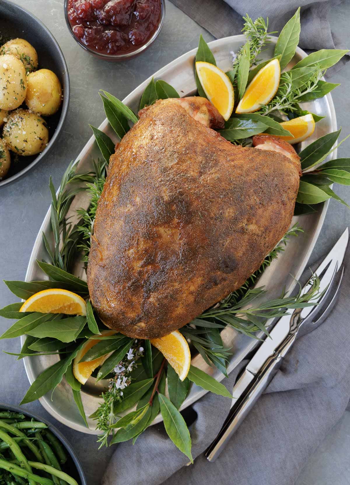 A whole smoked turkey breast on a pewter platter with fresh bay leaves and orange wedges. 