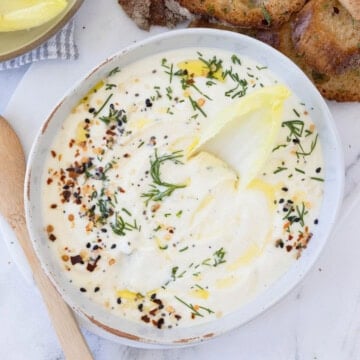 A bowl of whipped ricotta cheese dip with endive leaf in for scooping.