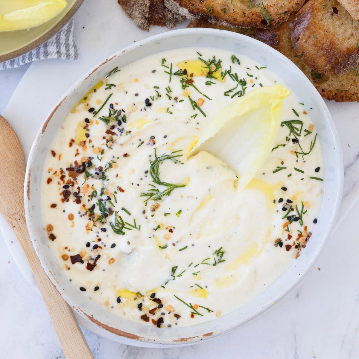 A bowl of whipped ricotta cheese dip with endive leaf in for scooping.