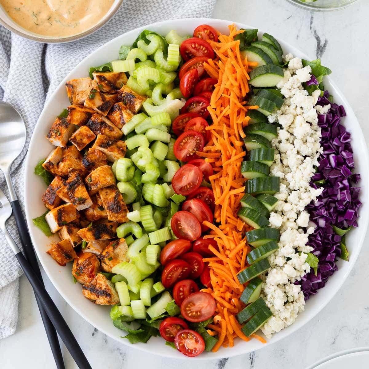 Colorful rows of buffalo chicken salad in a round bowl with creamy dressing on the side.